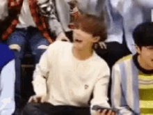 a group of young men are sitting in a row and one of them is holding a cell phone .