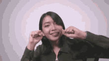 a woman in a green jacket is making a funny face while holding her ears .