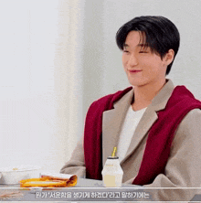 a young man is sitting at a table with a bottle of milk and a sandwich .