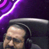 a man with a mustache and glasses is wearing headphones and sitting in a chair .