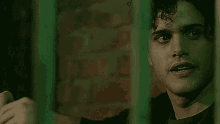 a man is behind bars in a prison cell and looking through the bars at the camera .