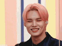a young man with pink hair is smiling and wearing earbuds