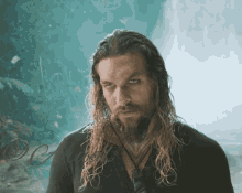 a man with long hair and a beard is standing in front of a waterfall with the letters dc behind him
