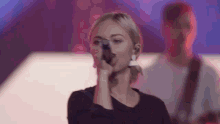 a woman singing into a microphone with a man in the background
