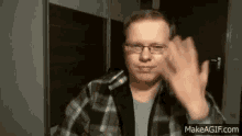 a man wearing glasses and a plaid shirt is waving