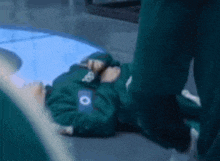 a person in a green suit is laying on the floor with a phone in their hand .