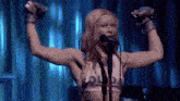 a woman is singing into a microphone with her arms in the air and a shirt that says gold on it