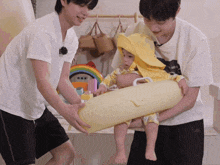 two men are holding a baby wearing a yellow hooded blanket and a yellow float