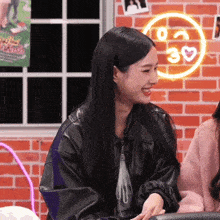 a woman in a black jacket smiles in front of a neon sign that says 30