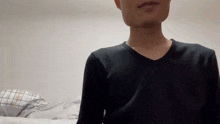 a man in a black shirt is standing in front of a bed with a pillow .
