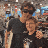 a man wearing sunglasses stands next to a woman wearing a black t-shirt that says olrink