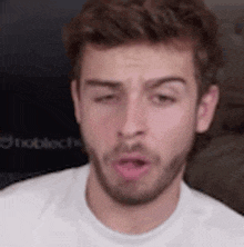 a close up of a man with a beard wearing a white t-shirt making a funny face .