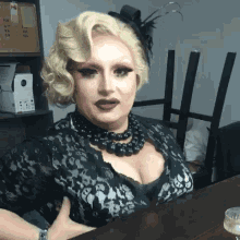 a woman sitting at a table wearing a black dress and a necklace