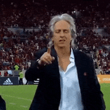 a man in a suit is standing on a soccer field giving a thumbs up .