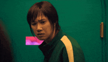 a woman in a green jacket with a white stripe on the side is standing in front of a green door
