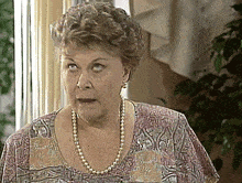 an older woman wearing a pearl necklace and earrings is looking at the camera
