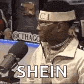 a man wearing a headband and glasses is sitting in front of a microphone and saying shein .