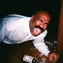 a man in a white shirt is laying on the floor with a bottle of hennessy in front of him