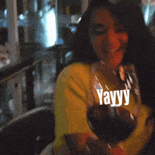 a woman in a yellow shirt is drinking a glass of wine and the word yayy is on the table