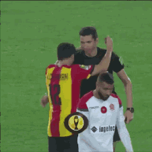 a man in a yellow and red jersey with the number 12 on it is talking to another man on a field .