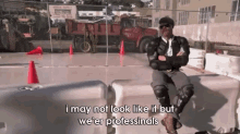a man in a suit is sitting on a barrier and says " i may not look like it but we 'er professionals "
