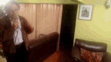 a man is standing in a living room with a couch and a picture on the wall .