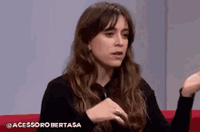 a woman is sitting on a red couch talking to someone while wearing a black shirt .