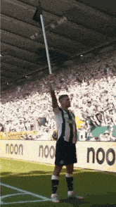 a soccer player is holding up a flag in front of a noon sign