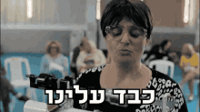a woman wearing glasses and a leopard print shirt is holding a machine with hebrew writing above it