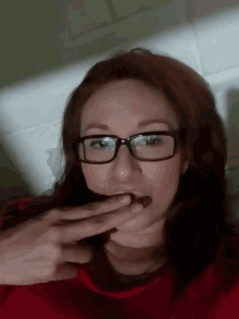 a woman wearing glasses and a red shirt is licking her lips