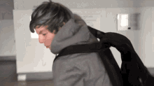 a person with blue hair is wearing a grey jacket and carrying a black backpack