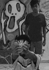 a black and white photo of two boys in front of a wall with graffiti