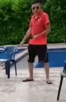 a man in a red shirt and black shorts is dancing in front of a pool .