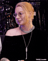 a woman wearing glasses , a necklace and hoop earrings is smiling .