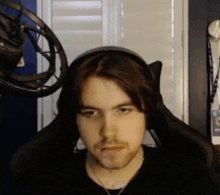 a man wearing headphones is sitting in front of a microphone and looking at the camera .
