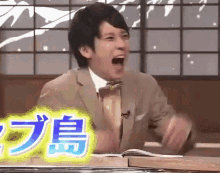 a man in a suit and tie is laughing while sitting at a table with chinese writing on it .