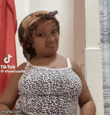 a woman wearing a leopard print tank top and a head scarf is standing in front of a shower curtain .