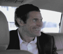 a man in a suit and white shirt is smiling in the back seat of a car