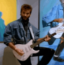 a man in a denim jacket is playing a guitar with the letter h on the neck