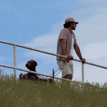 a man standing next to a railing with a dog on a leash behind him