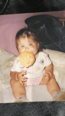 a baby in a pink and white outfit is holding a cookie