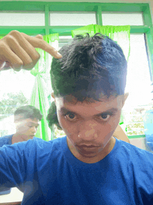 a young man in a blue shirt points to his hair