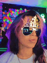 a woman wearing a crown and sunglasses looks at the camera