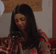 a woman is sitting on a couch looking at her phone .