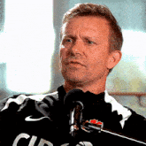 a man wearing a black and white shirt with the word canada on it stands in front of a microphone