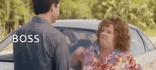 a man and a woman are standing next to each other in front of a car and the woman is yelling at the man .