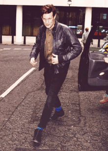 a man wearing a leather jacket and blue socks walks down a street