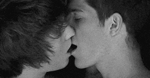 a black and white photo of two young men kissing each other .