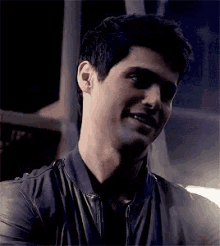 a close up of a man wearing a leather jacket and smiling at the camera .
