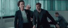a man and a woman in suits are walking through a room with other people .